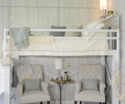 A side angle view of a full size white Adult Loft Bed focused on the bunk. Two grey chairs beneath the bed with a gold table between them.