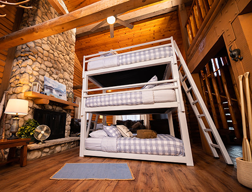 A white queen size Triple Bunk Bed for adults in a beautiful cabin seen from the lower right hand corner at a low angle.