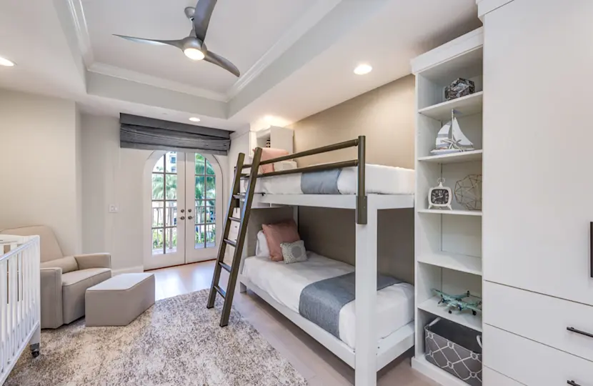 A white Adult Bunk Bed with a light bronze guard rail and ladder seen from the lower left-hand corner of the bed in an upscale bedroom in a Florida vacation home.