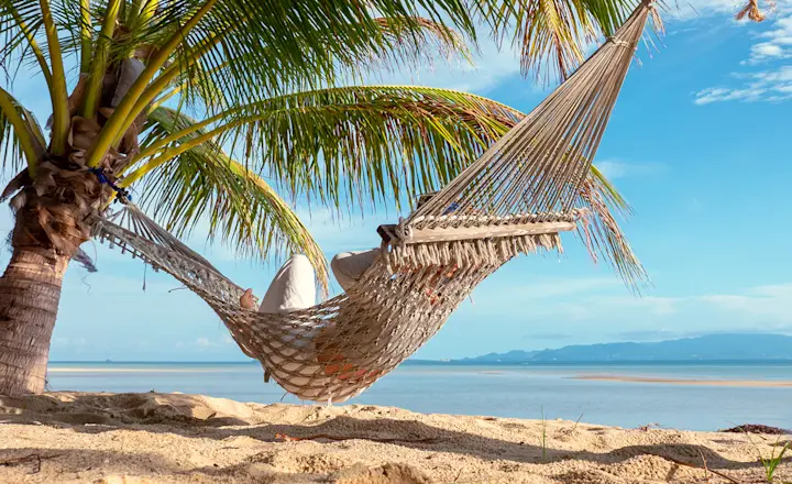 Woman lying in a hammock on a beach in Thailand seen from behind at a distance.