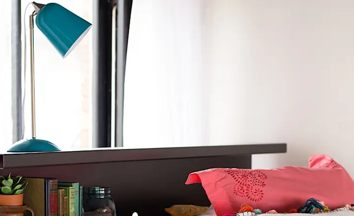 A blue lamp sits atop a charcoal bookshelf accessory on the top bunk of a Queen Over Queen Adult Bunk Bed