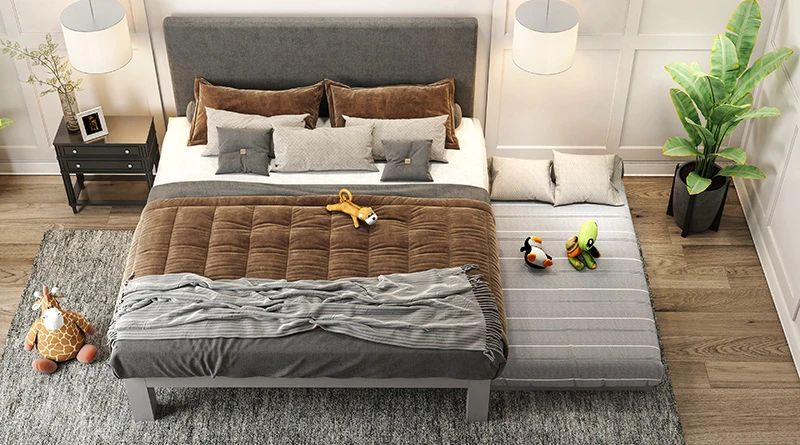 A light gray colored King size metal Platform Bed in the bedroom of parents of a young kid. The bed has a trundle attachment that is pulled out to show a dressed and made mattress with some stuffed animals lying on it.