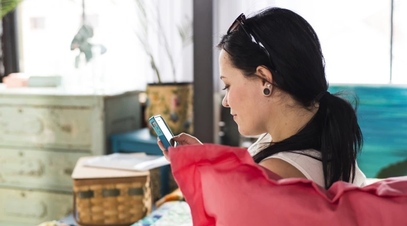 A young adult woman sitting on the bottom bunk of a charcoal Adult Bunk Bunk looking at her smartphone.