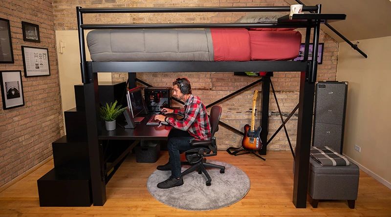 An adult male gamer playing on his computer underneath his black Queen Adult Loft Bed.