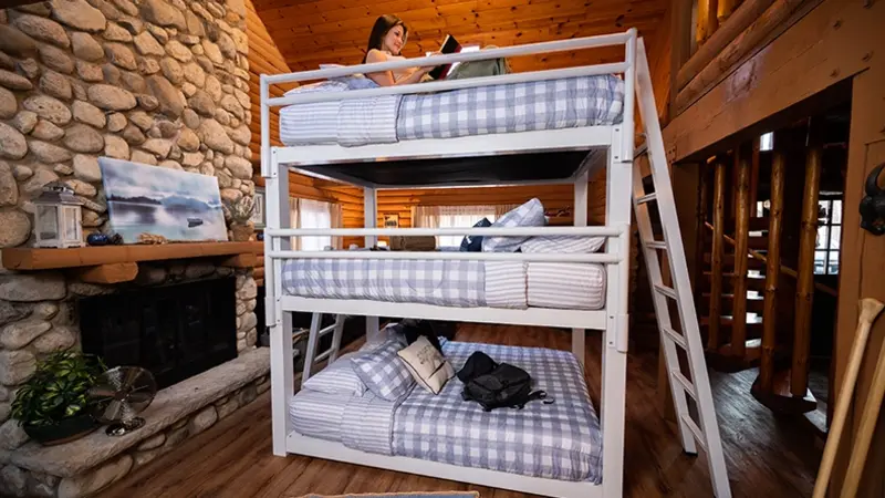 White Queen Triple Bunk Bed for adults with a young woman sitting on the top book reading a book seen from a slight angle at the left-hand side of the bed