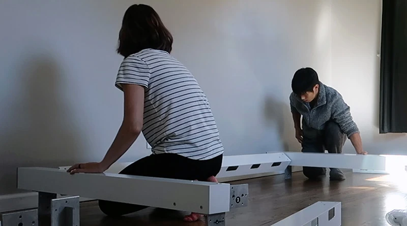 Heather from the US Japan Fam blog and her husband crouched over the floor assembling a white Twin Adult Loft Bed in their kids' room.