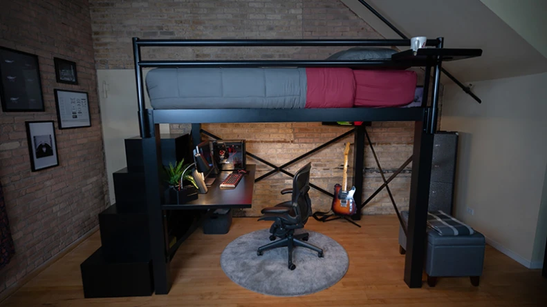 Queen Size Adult Loft Bed with a staircase and attached desk in an urban studio apartment with dark lighting seen directly from the left-hand side of the bed with the guard rail.