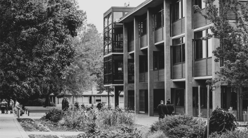 A black and white shot of students walking outside of a dormitory on a college campus.