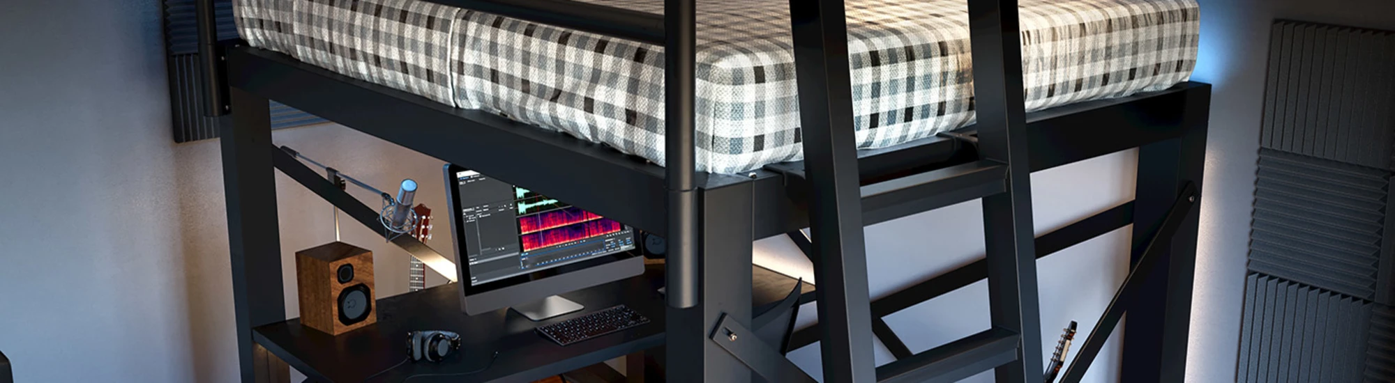 A loft bed with a checkered duvet is above a workspace with a desk, computer monitor, speakers, headphones, and keyboard. Soundproof panels adorn the walls, and a wooden floor completes the cozy setup.
