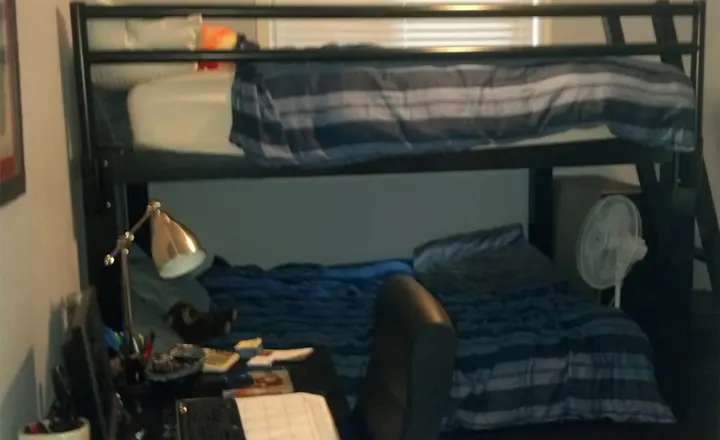 A black Full Over Full Adult Bunk Bed in a messy college dorm room