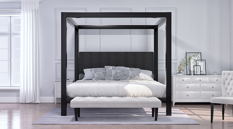 A black Wyoming King size Canopy Bed frame in a light, airy, and sparsely decorated bedroom seen directly from the foot of the bed.