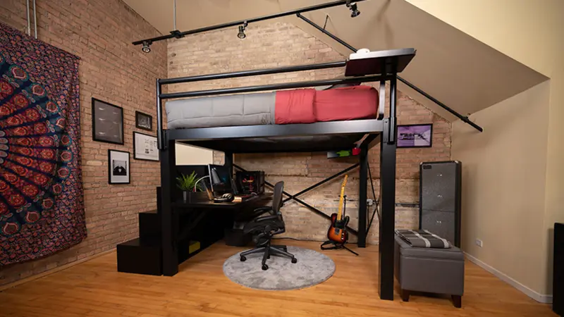 A black queen size Adult Loft Bed with a gamer setup underneath seen from the side at a wide, low angle.