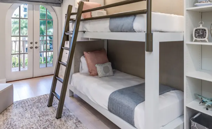 A white Queen Over Queen Adult Bunk Bed with a light bronze ladder and side rail in the guest room of a professionally decorated home in Naples, Florida.