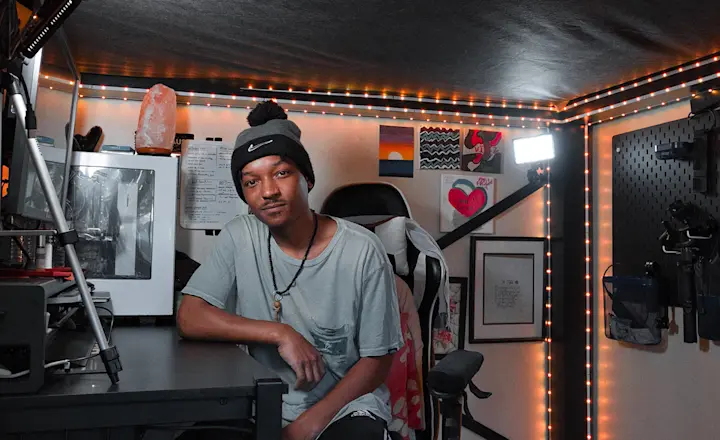 Young man sitting at his black desk underneath the frame of his black queen size Adult Loft Bed and looking at the camera.
