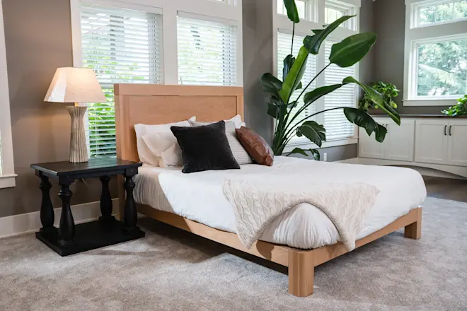 Solid wood platform bed with a wood headboard and layered bedding in a warm, bright bedroom