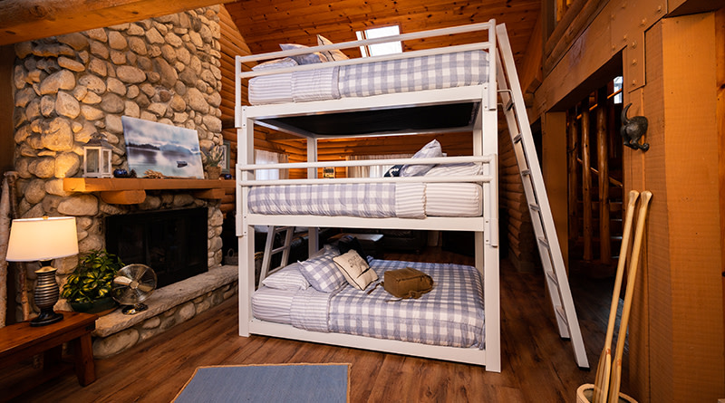 An unoccupied white Queen Size Triple Bunk Bed with bags on the bottom bunk in a high end vacation cabin.
