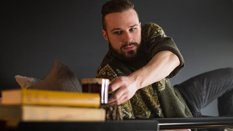 Adult man sitting on the top bunk of a black Adult Bunk Bed reaching for his coffee mug sitting on the attached tray.