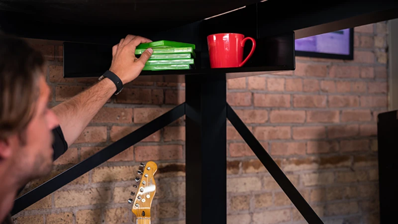 Adult man reaching for a video game case sitting on the below-the-frame Corner Shelf attached to his black queen size Adult Loft Bed.
