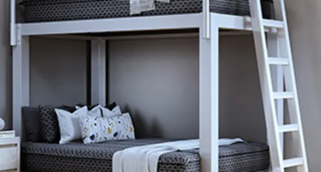 Jameson-style (dark gray with white patterning) zipper bedding on a white Full XL Over Queen Adult Bunk Bed seen at a distance from the lower right-hand corner.