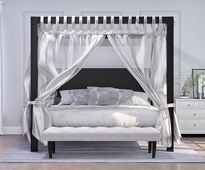 A charcoal Wyoming King size Canopy Bed with white drapes in a light, sparsely decorated but upscale bedroom. Seen directly from the foot of the bed.