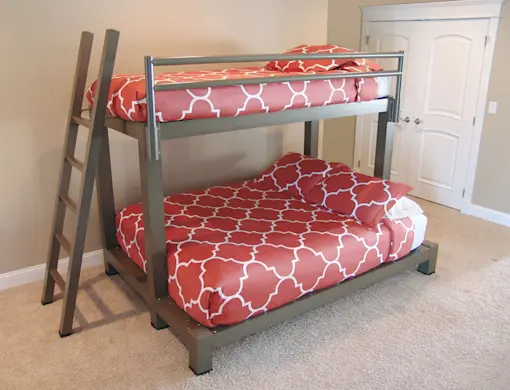A bunk bed with a metal frame and a ladder is placed in a carpeted room. The upper and lower beds have matching red and white patterned bedding. A closed white double door is visible in the background.