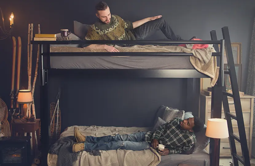 Two adult men on both bunks of a black Queen Over Queen Adult Bunk Bed in a ski lodge vacation rental looking at one another.
