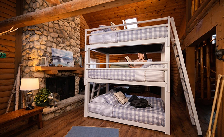 Young woman lying on the middle bunk of a white Triple Bunk Bed for Adults in a luxury cabin setting reading a book and seen from a slight distance at a low angle.