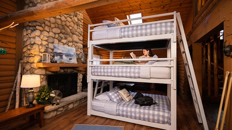 Young woman lying on the middle bunk of a white Triple Bunk Bed for Adults in a luxury cabin setting reading a book and seen from a slight distance at a low angle.