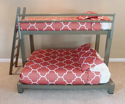 A bunk bed with a metal frame and an angled ladder. The top bunk is a twin size and the lower bunk is full size, both featuring orange and white geometric patterned bedding against a neutral wall and carpeted floor.