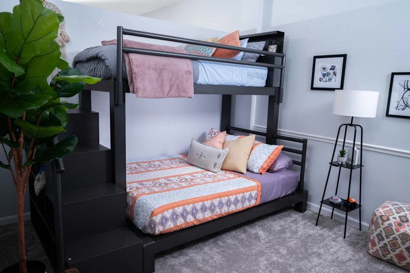 Charcoal Adult Bunk Bed in a simple guest room with a matching wooden staircase, bookshelf headboard, and pillow support. Seen from the lower left-hand corner of the bed.
