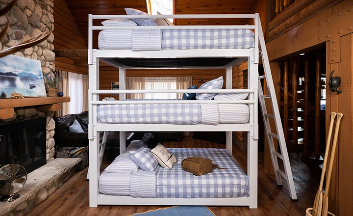 White Triple Bunk Bed for adults inside of an upscale, rustic cabin seen directly from the right-hand side of the bed with the guardrails.