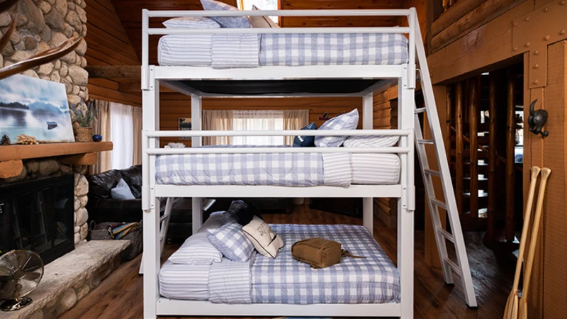 White Triple Bunk Bed for adults inside of an upscale, rustic cabin seen directly from the right-hand side of the bed with the guardrails.