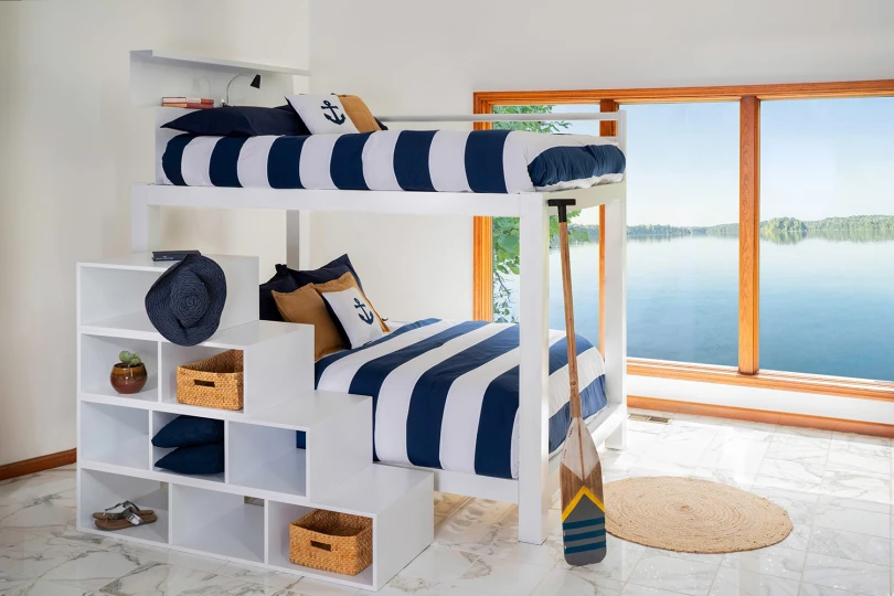 A white Adult Bunk Bed in a lake house bedroom with a matching wooden staircase. Dressed in blue and white striped bedding.