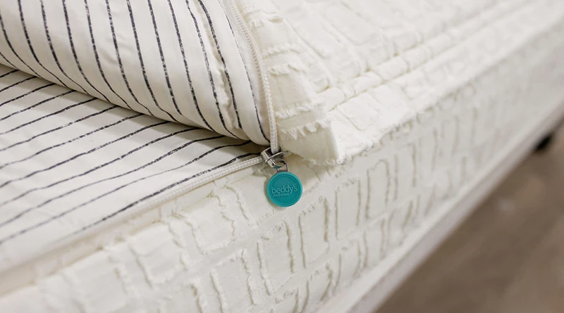 London-style (cream colored with rectangular patterning) zipper bedding partially unzipped to reveal the bottom layer sheet and very zoomed in on the zipper.