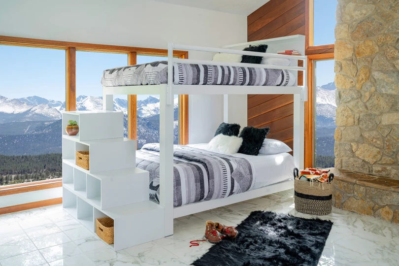 A white Queen Over Queen Bunk Bed for adults with blue and grey bedding and matching staircase in a mountain home guest bedroom. 