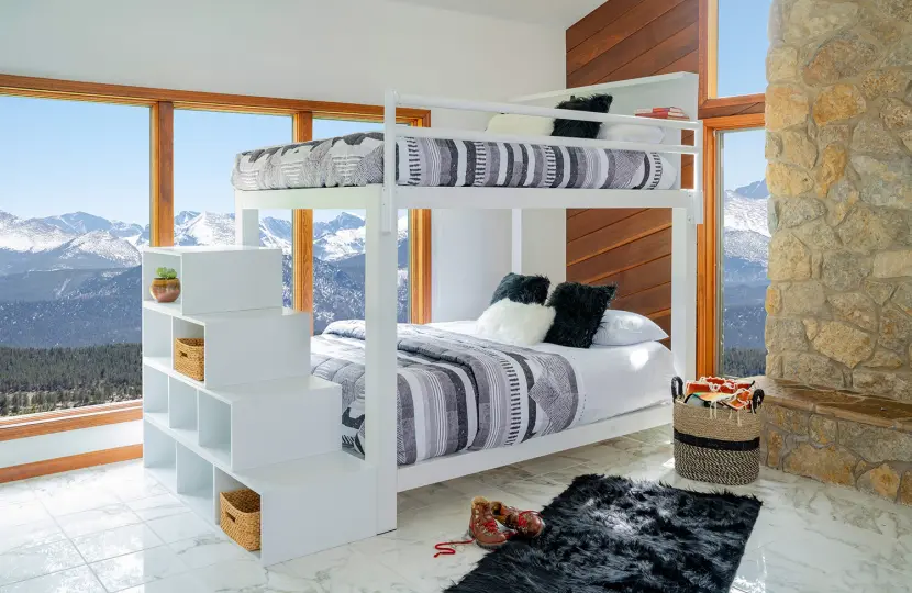 A white Queen Over Queen Bunk Bed for adults with blue and grey bedding and matching staircase in a mountain home guest bedroom. 