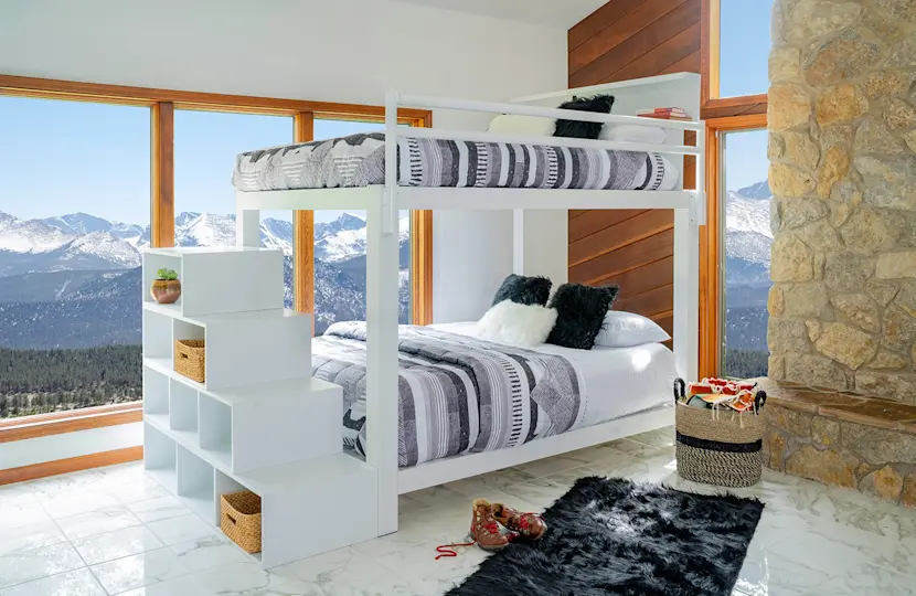 A white Queen Over Queen Bunk Bed for adults with blue and grey bedding and matching staircase in a mountain home guest bedroom.