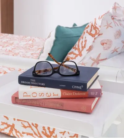 A close up shot of a white tray accessory with three books and a pair of eyeglasses stacked on it attached to the top bunk of an Adult Bunk Bed.