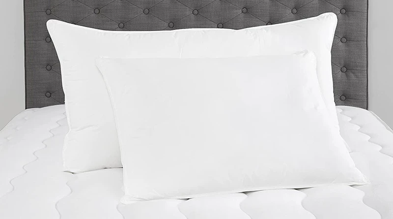 Two Chamber Down Pillows (one king size and one standard size placed in front of it) resting on an unmade mattress on a bed with a dark gray headboard.