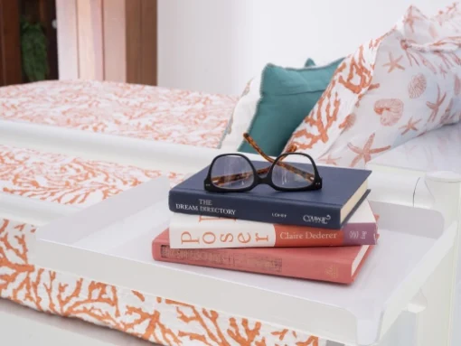 Close up of a pair of glasses resting on top of three hardcover books on a white tray accessory attached to the top bunk of a white Queen Over Queen Adult Bunk Bed.