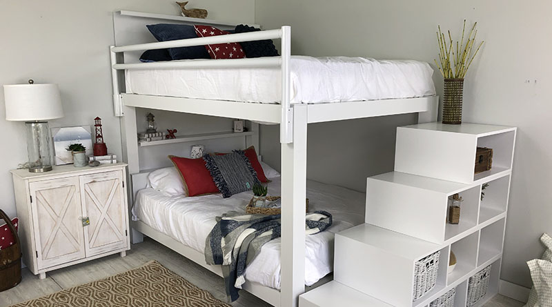 A white Queen Over Queen Adult Bunk Bed with a matching staircase accessory decorated in red, white, and blue themed bedding and decor.