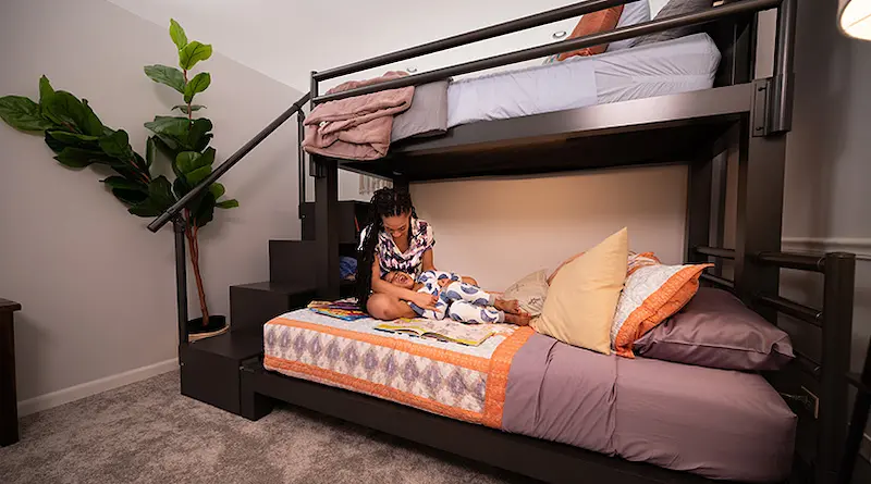 A young mother and her son playing and laughing on the bottom bunk of a charcoal Twin XL Over Queen Adult Bunk Bed with a staircase in their pajamas before bed.