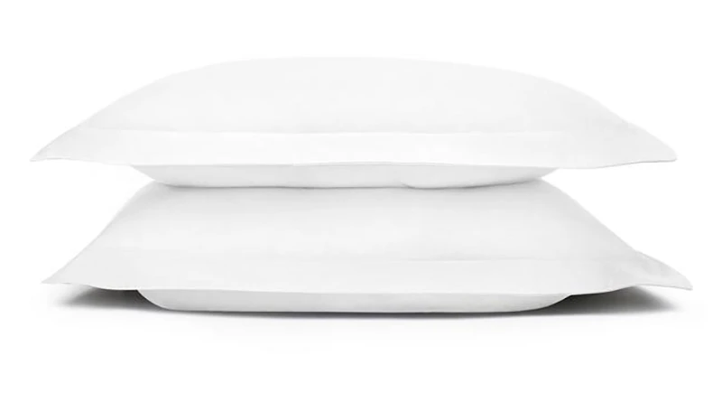 Two pillows covered in white pillow shams stacked on top of one another over a white background