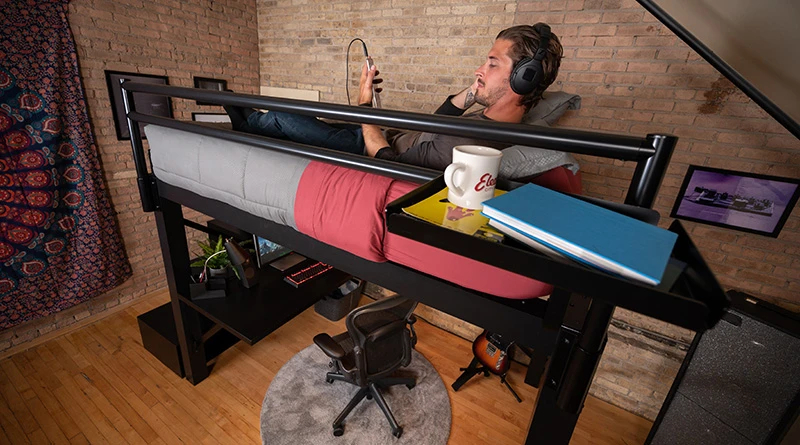 A large young man laying in his black queen size Adult Loft Bed listening to music on his phone.