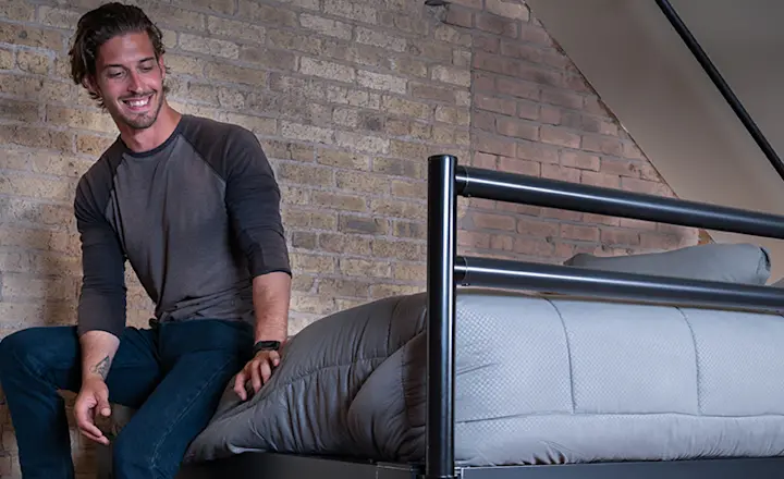 A young adult man sitting on the edge of his black Queen Adult Loft Bed resting his feet on the staircase