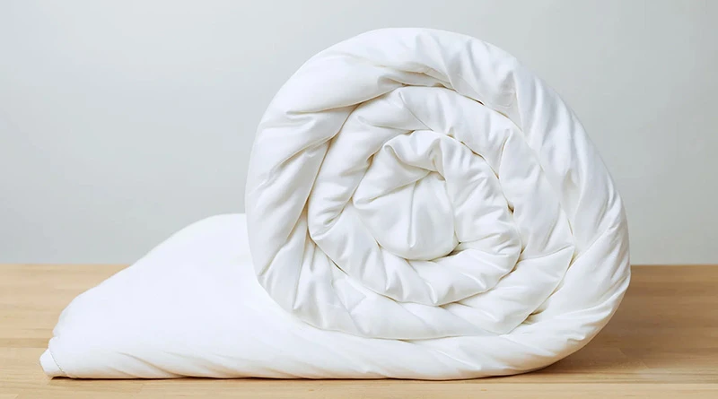 A white duvet insert rolled up on a wooden table against a blank background.