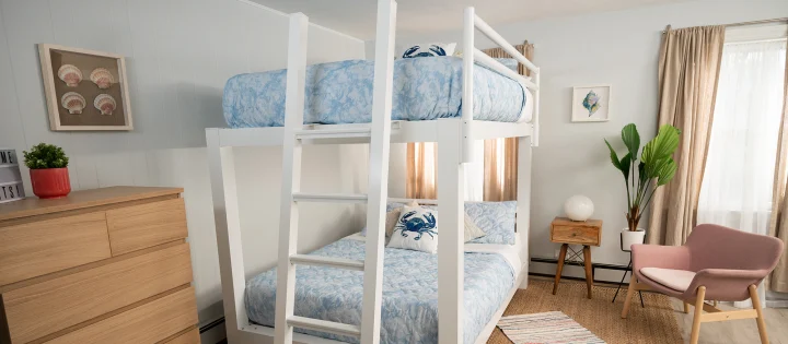 White Queen Over Queen Bunk bed For Adults in a beach house bedroom with light blue and white bedding on both bunks. Seen from the foot of the bed at a sllight angle towar the lower left-hand corner of the bed.