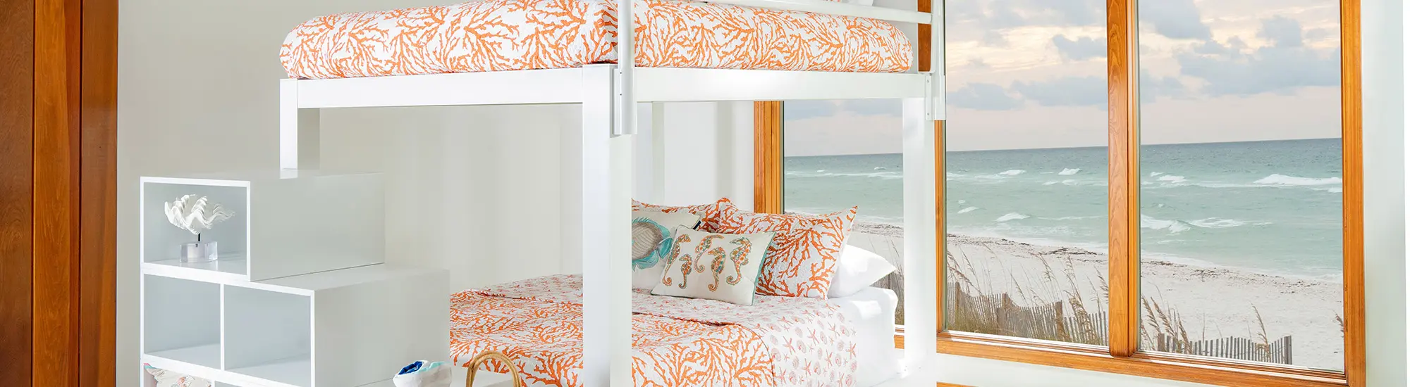 White Queen over Queen Adult Bunk Bed with Wooden Staircase at the end of the bed frame in a sparsely decorated beach house bedroom seen from the left-hand side of the bed.