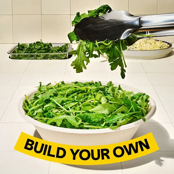 Tongs placing arugula into a bowl. Text on the image says, "Build Your Own". 