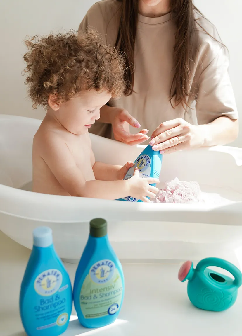 Baby in der Badewanne hält Penaten Creme in den Händen